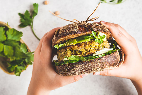 Bilde av to hender som holder en plantebasert burger i hånden. Med hvit bakgrunn og salat.